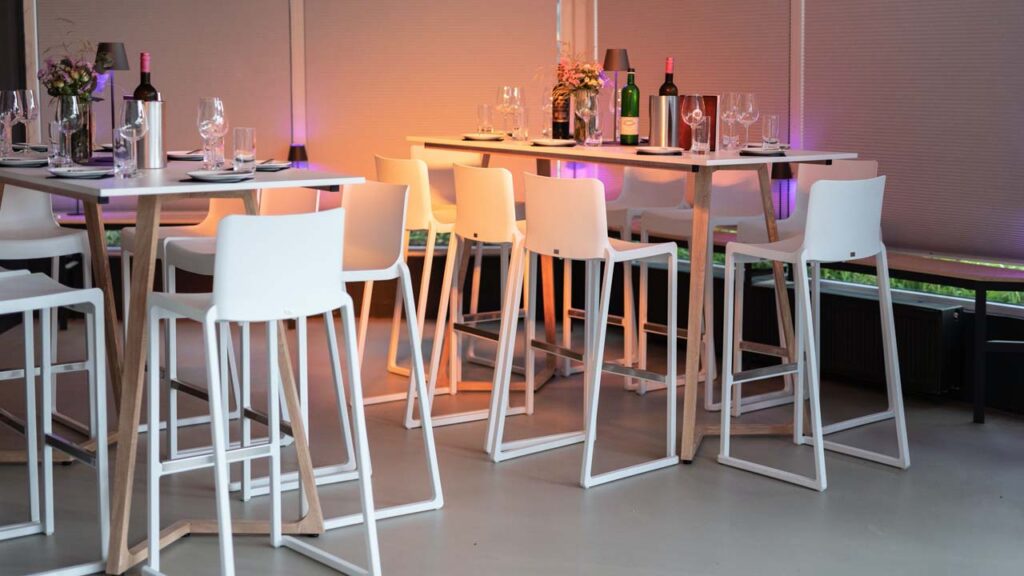 weiße Sitzgruppen aus Hochtischen und Barhockern im Wintergarten der amSee Location.