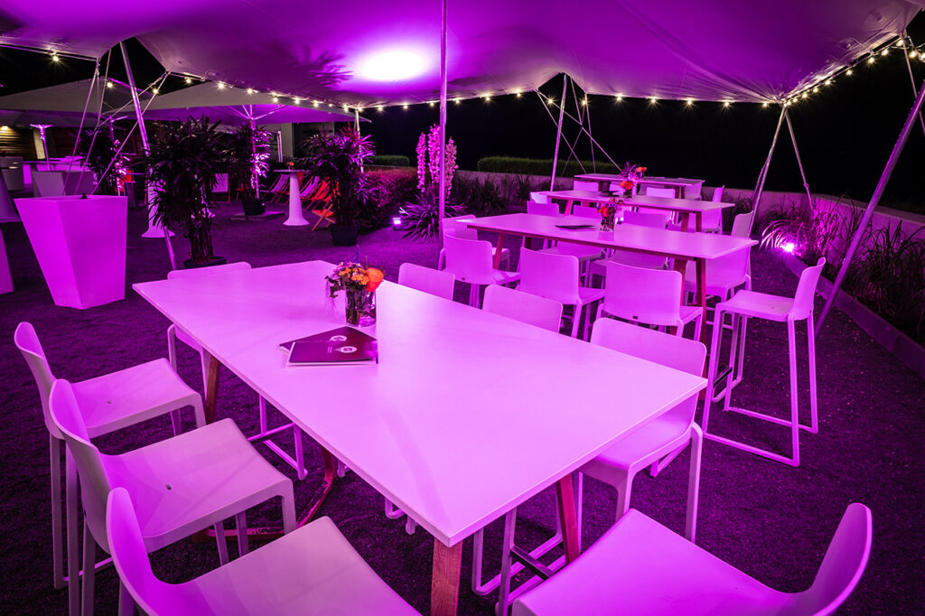 Außenbereich der Location mit Sitzgruppen unter einem Sonnensegel. Lilafarbene Beleuchtung sorgt für besondere Akzente am Abend.