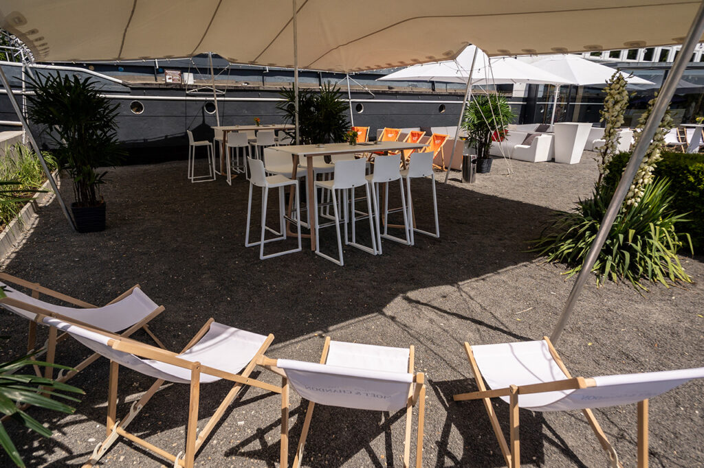 Sitzgruppe und Liegestühle unter einem großen Sonnensegel vor dem Bug der amSee Eventlocation.