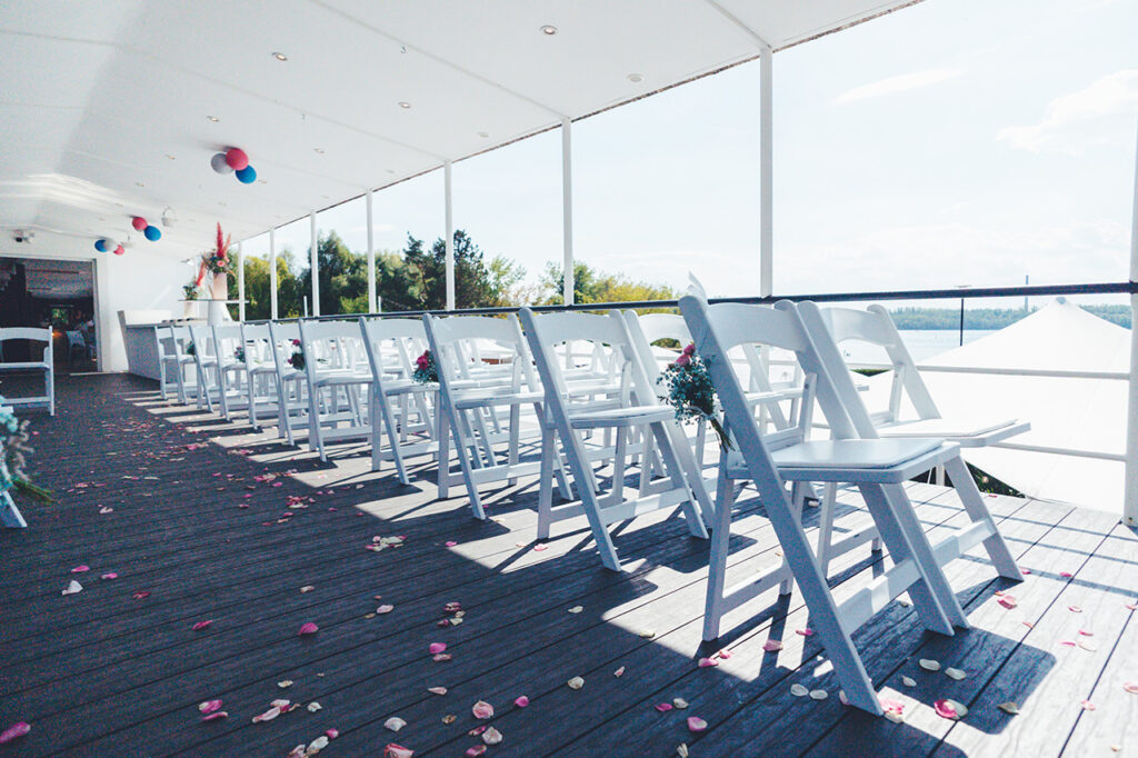 Die Oberdeck-Terrasse des amSee mit Bestuhlung für eine Freie Trauung: weiße Vintagestühle in Reihen.