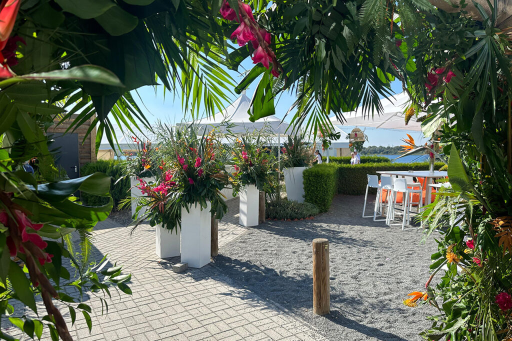 Blick von Eingang in Richtung See, der Außenbereich der Location ist für eine Hochzeit üppig mit Blumenarrangements dekoriert.