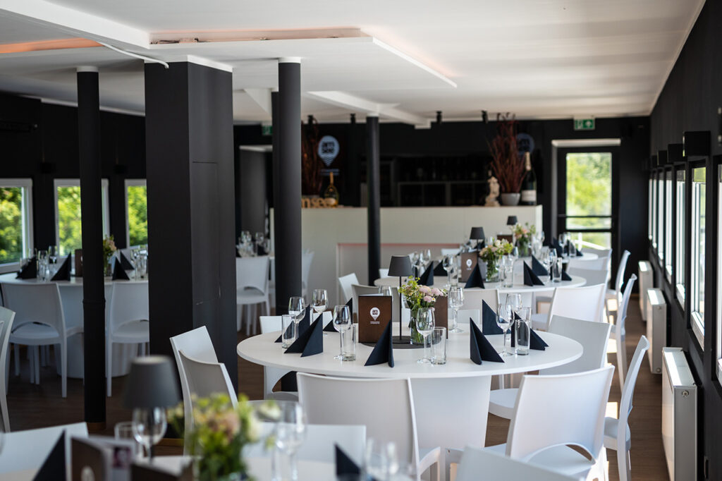 Gedeckte weiße Tische im Oberdeck, im Hintergrund die Bar. Für Kontraste sorgen die schwarzen Wände und Servietten auf den Tischen.