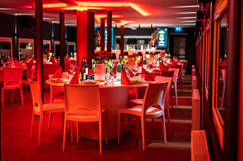 Das in festlichem Rot beleuchtete Oberdeck der Eventlocation amSee am Abend. Eingedeckt ist für eine Weihnachtsfeier.