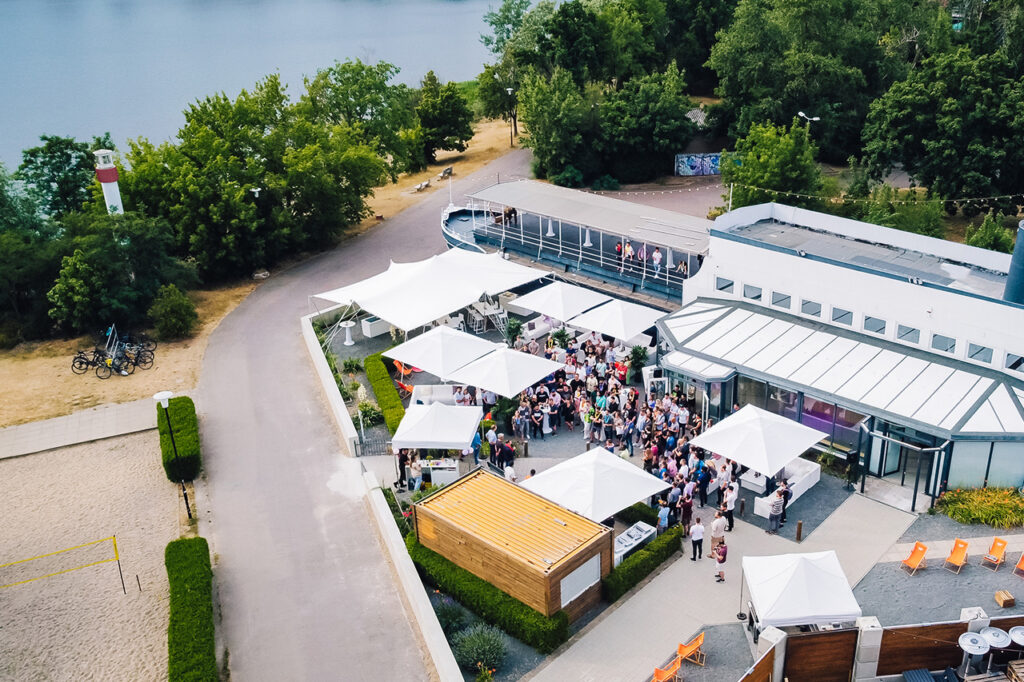 amSee Eventlocation von oben während einer Firmenfeier. Viele Menschen befinden sich im Außenbereich, einige auch auf der Oberdeck-Terrasse.