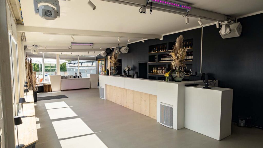 Der Wintergarten mit der großen Hauptbar. Für Akzente sorgen die schwarze Wand hinter der Bar sowie der Tresen in Weiß mit Holzelementen.