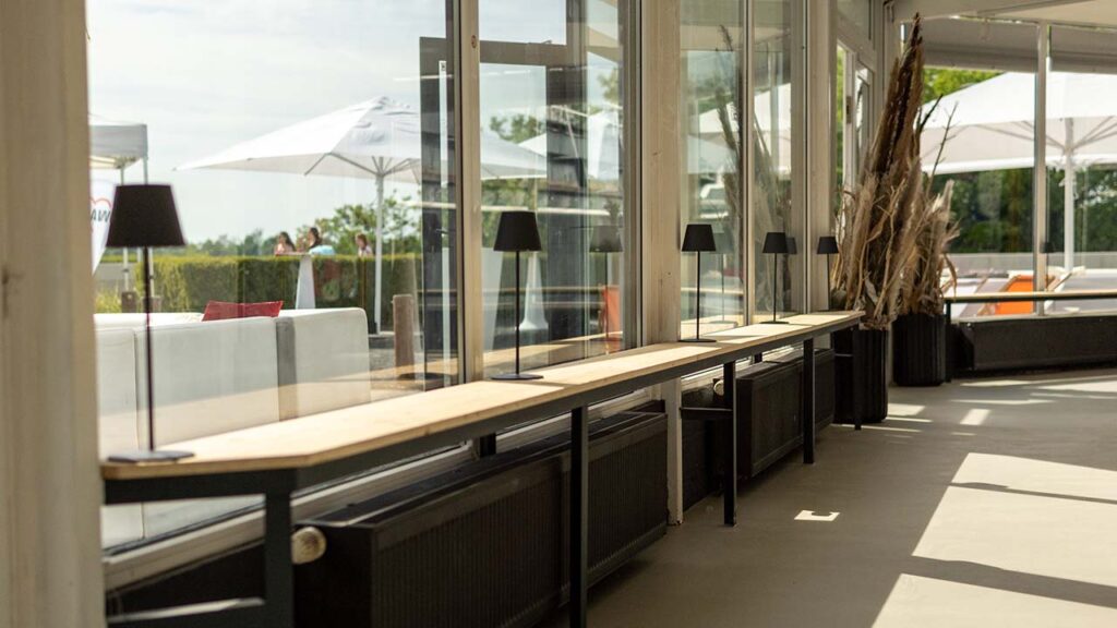 Sitzbänke vor den großen Fenstern des Wintergartens, im Hintergrund der Außenbereich im Sonnenschein.