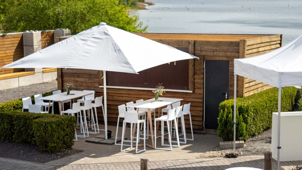 Sitzgruppen vor dem Bar-Container im Außenbereich der amSee Location, Im Hintergrund der See.