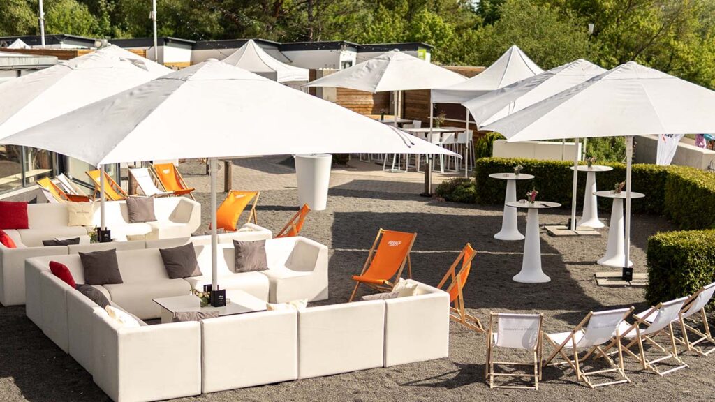 Liegestühle und Sitzgruppen im Außenbereich der amSee Location, im Hintergrund Bäume.