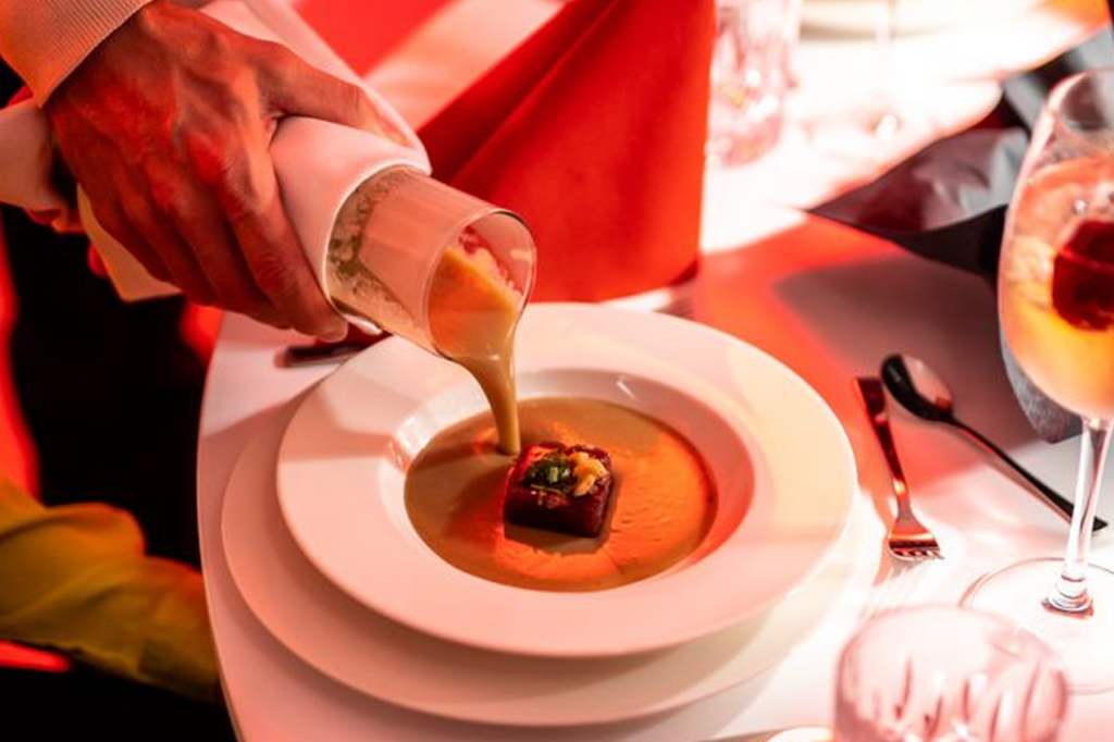 Aus einer Karaffe wird Suppe auf einen vorbereiteten Teller gegossen.