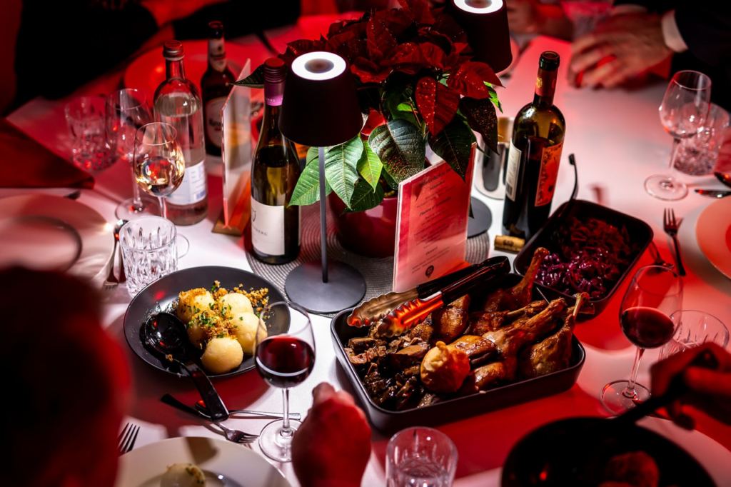 Ein weißer Banketttisch, auf dem neben Gedecken auch dunkle Schalen mit Gänsekeulen, Knödeln und Beilagen stehen.